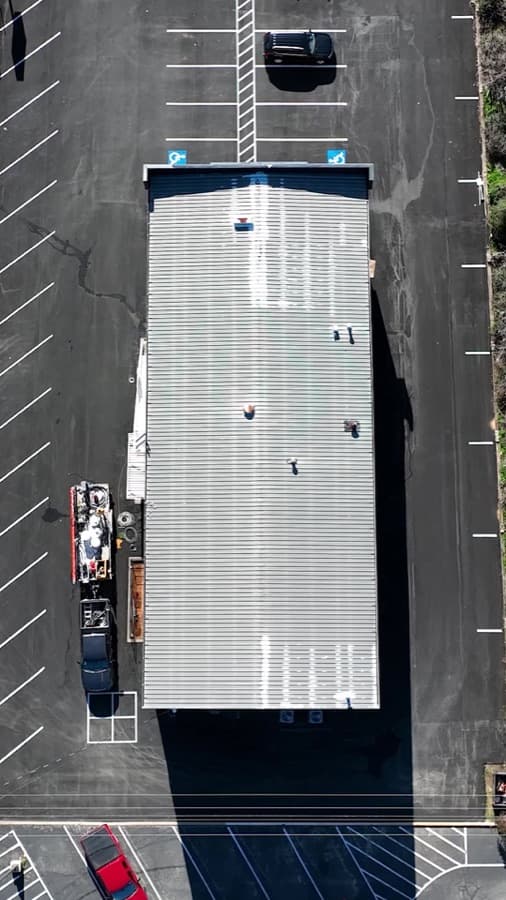 Aerial reference view of a low-slope commercial metal building roof with penetrations and perimeter drainage context